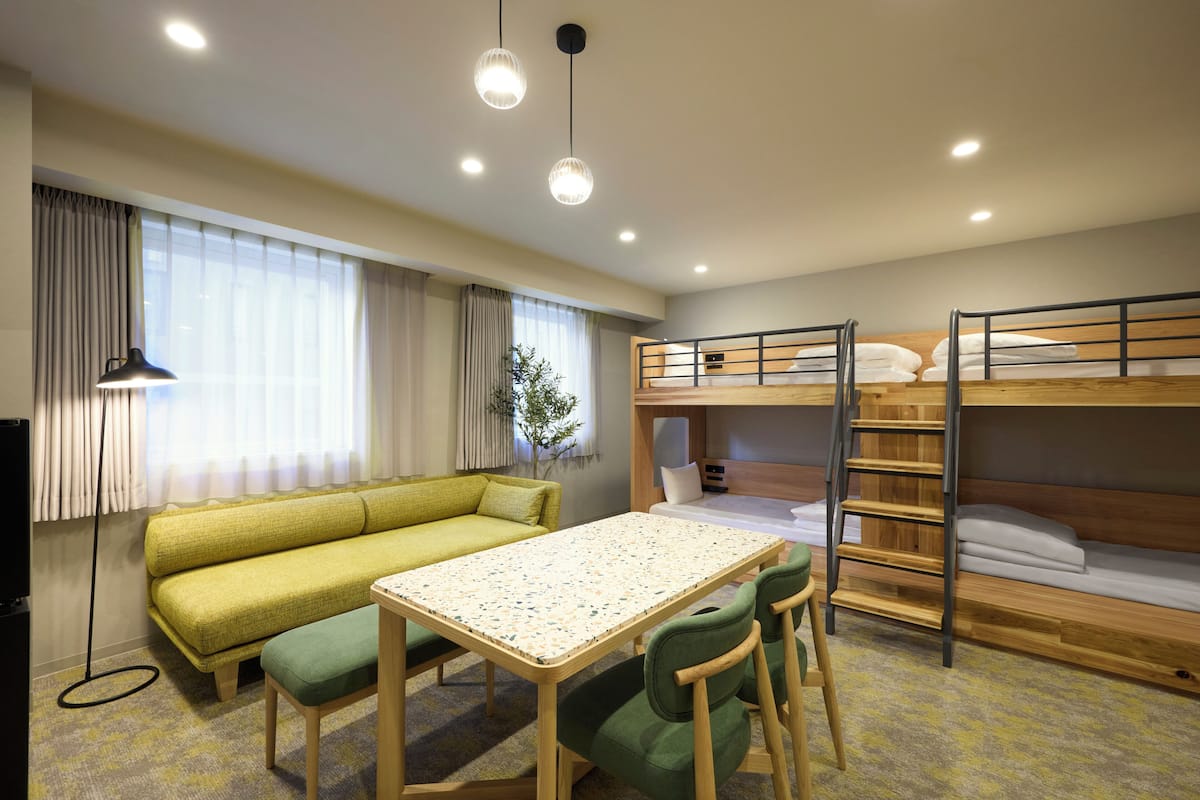 Una habitación con una cama litera, un sofá, una mesa, sillas, una lámpara y una planta.