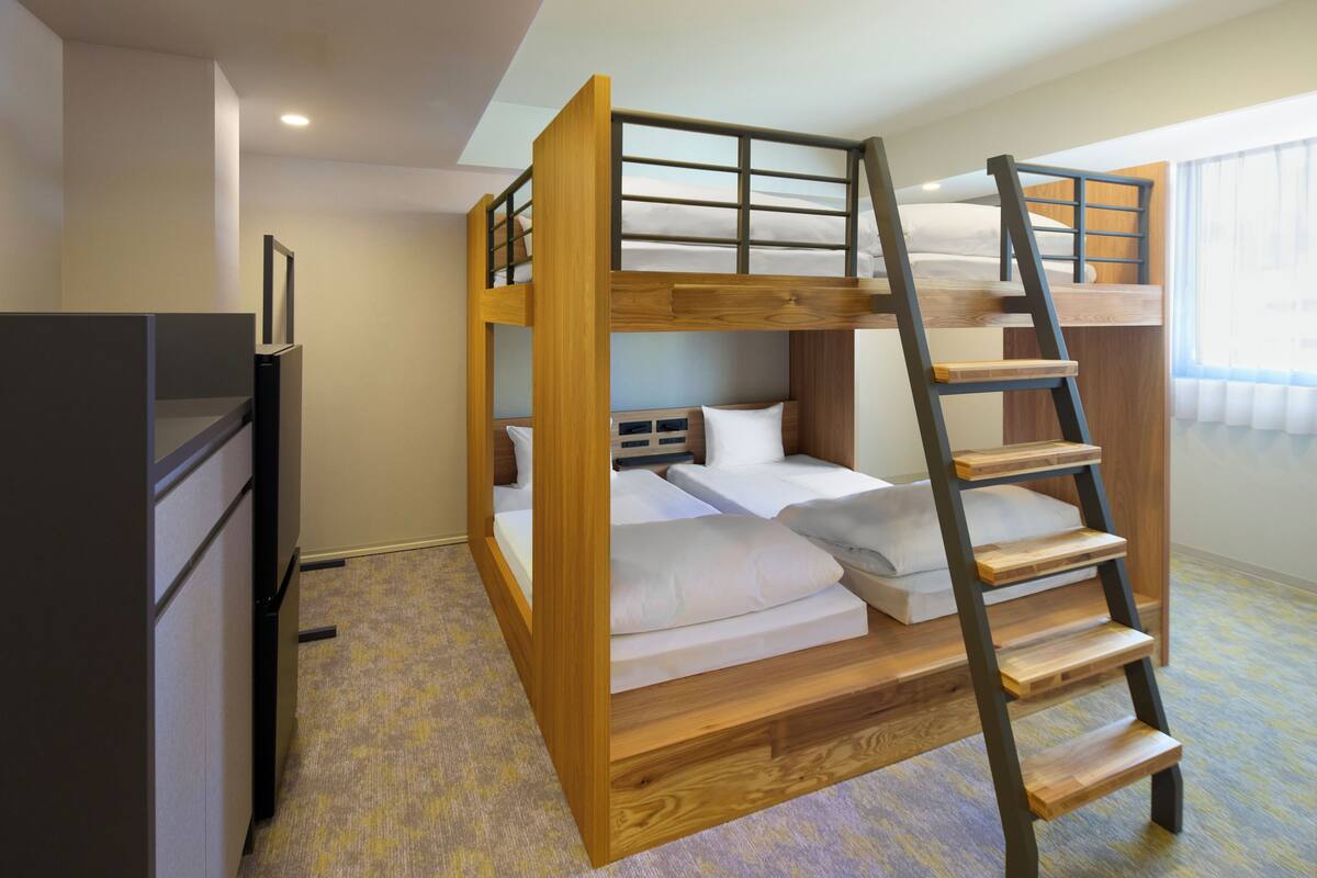 Habitación con literas, una escalera de madera, un escritorio y una ventana con cortinas.