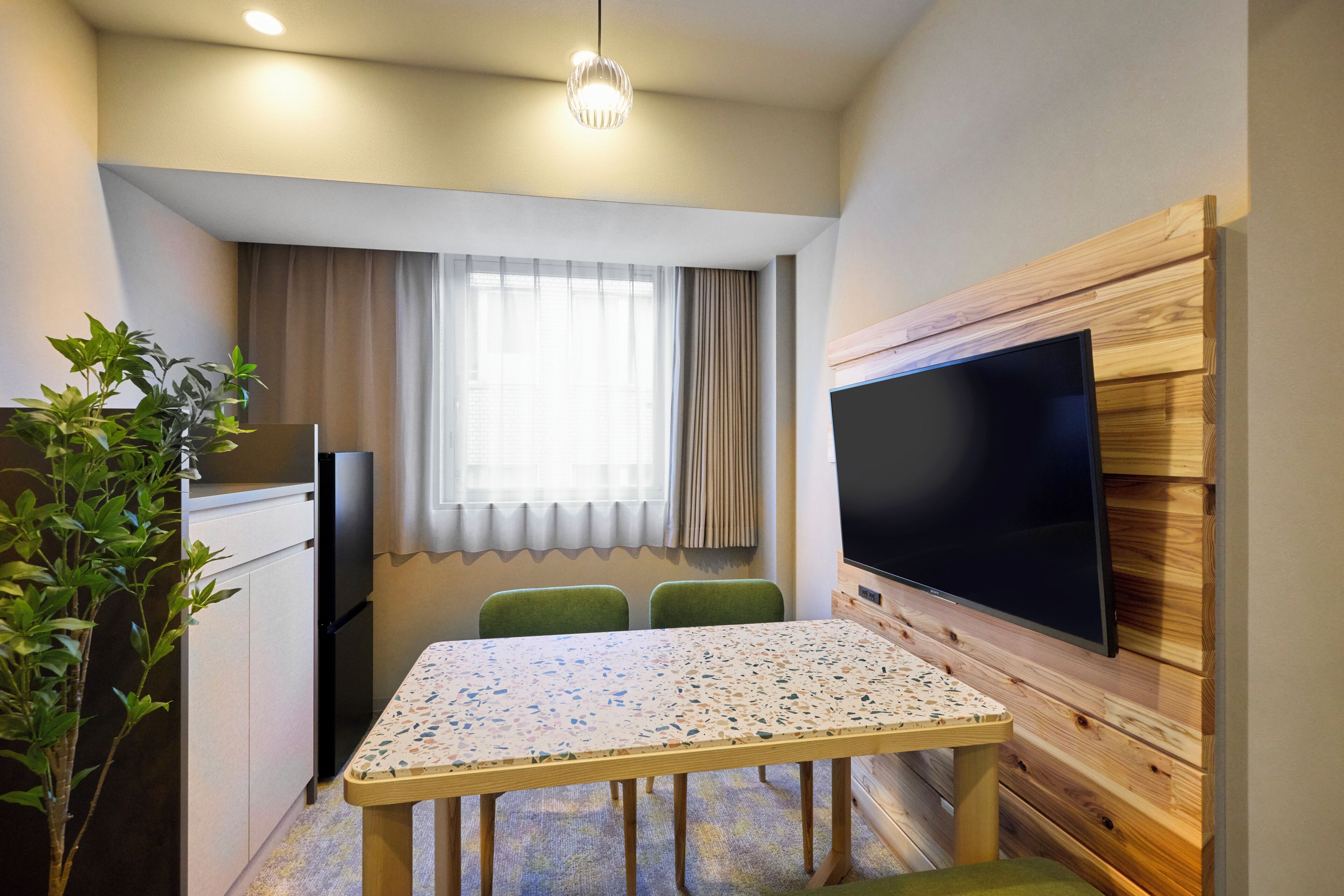 Um espaço de estar compacto com cozinha compacta, uma mesa de jantar, uma TV de tela plana fixada em uma parede de madeira e um vaso de planta.