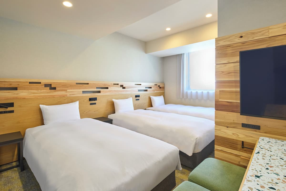Habitación de hotel con tres camas, un televisor, un escritorio y una ventana.