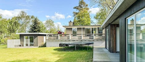 Ein modernes Haus mit einer Terrasse, einem kleinen Schuppen und einem großzügigen Raum mit vielen Fenstern.