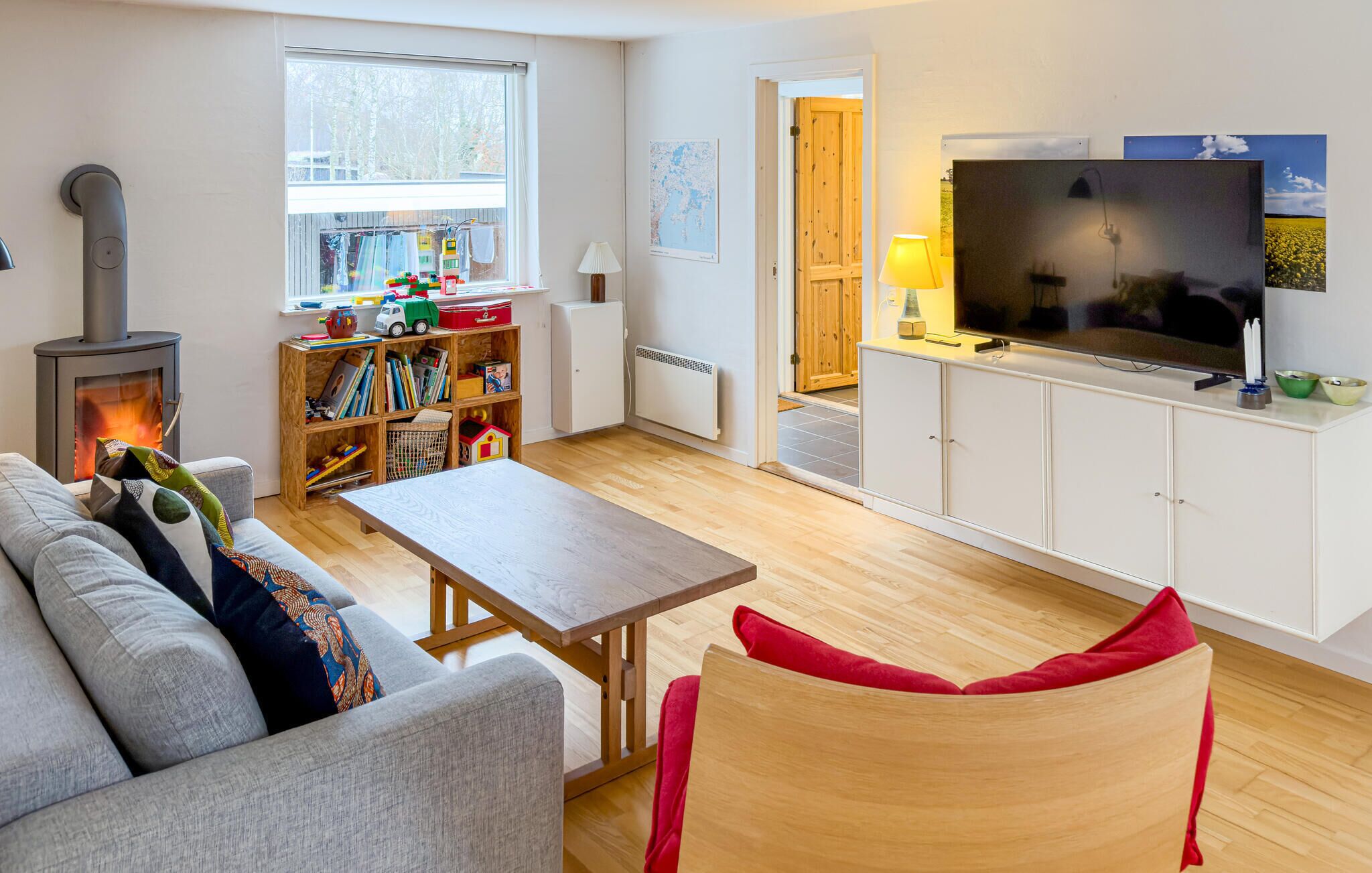 A cozy living room with a sofa, a wooden table, a TV, and a bookshelf filled with children's toys.