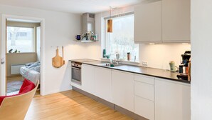 A modern kitchen with white cabinets, a built-in oven, and a window with a view of trees. - 4 bedroom beautiful home in Knebel (Knebel)