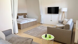 Une chambre d’hôtel moderne équipée d’un lit, d’un canapé, d’une petite table ronde avec une télécommande et un verre, et d’un téléviseur fixé au mur.