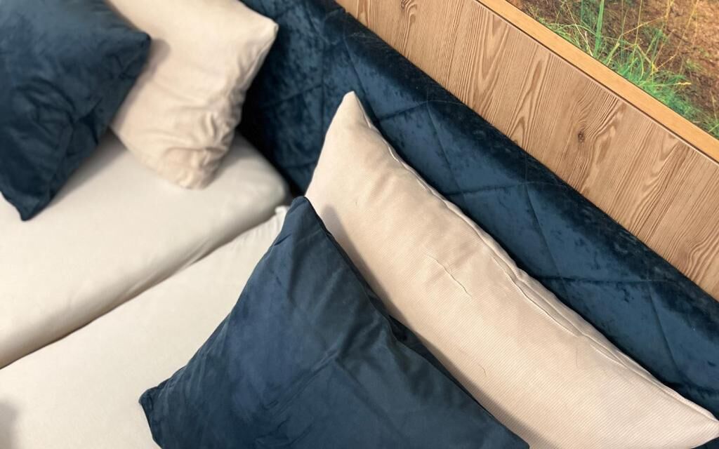 Een bed met een donkerblauwe hoofdbord en meerdere kussens in blauw- en beigetinten.