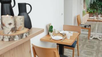 Een eethoek met houten tafels en stoelen, een koffiepot en een karaf op het aanrecht.
