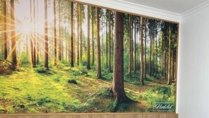 Une chambre d’hôtel avec deux lits, une grande fresque représentant une forêt sur le mur et une tête de lit en bois.