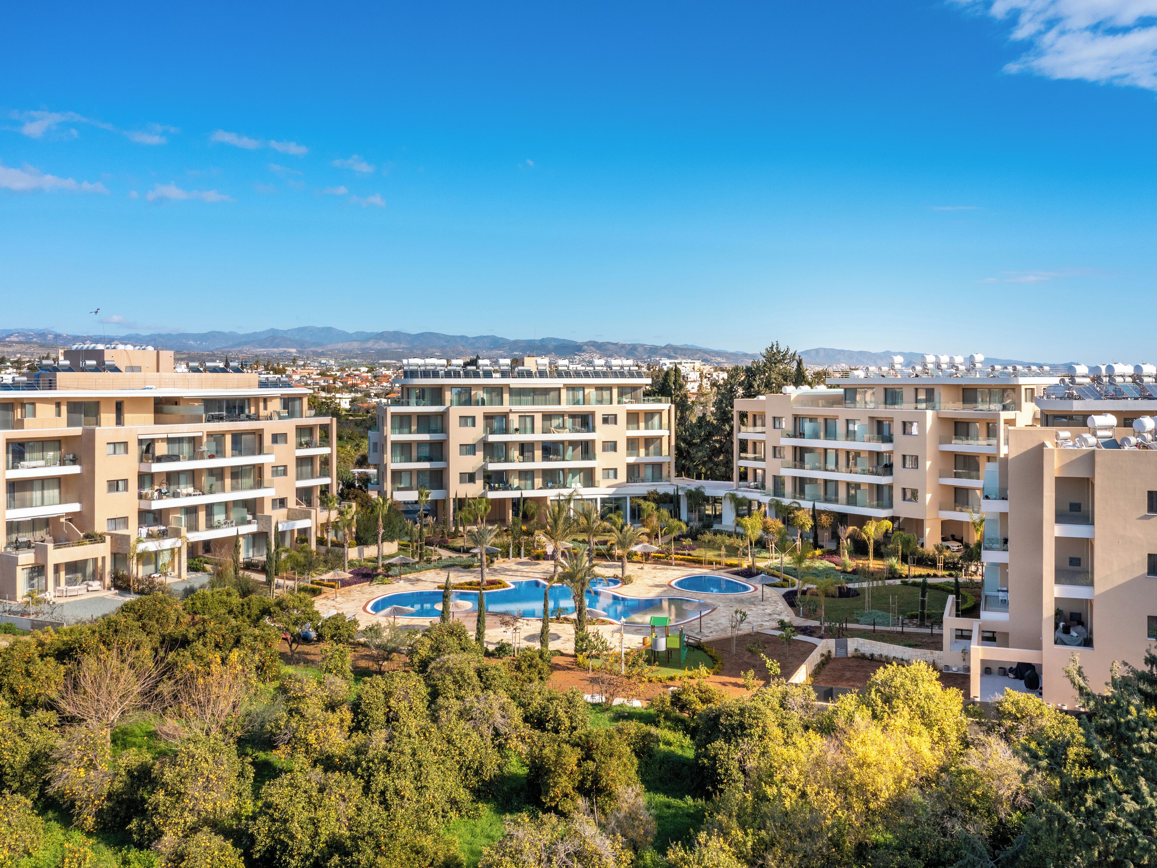 A modern apartment complex with multiple buildings, a central swimming pool, and surrounding greenery.