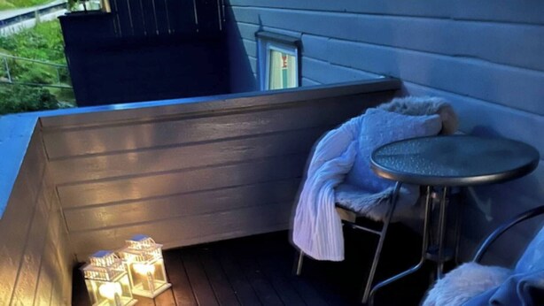 Une terrasse en bois avec une table et des chaises en métal, un banc et deux lanternes allumées.