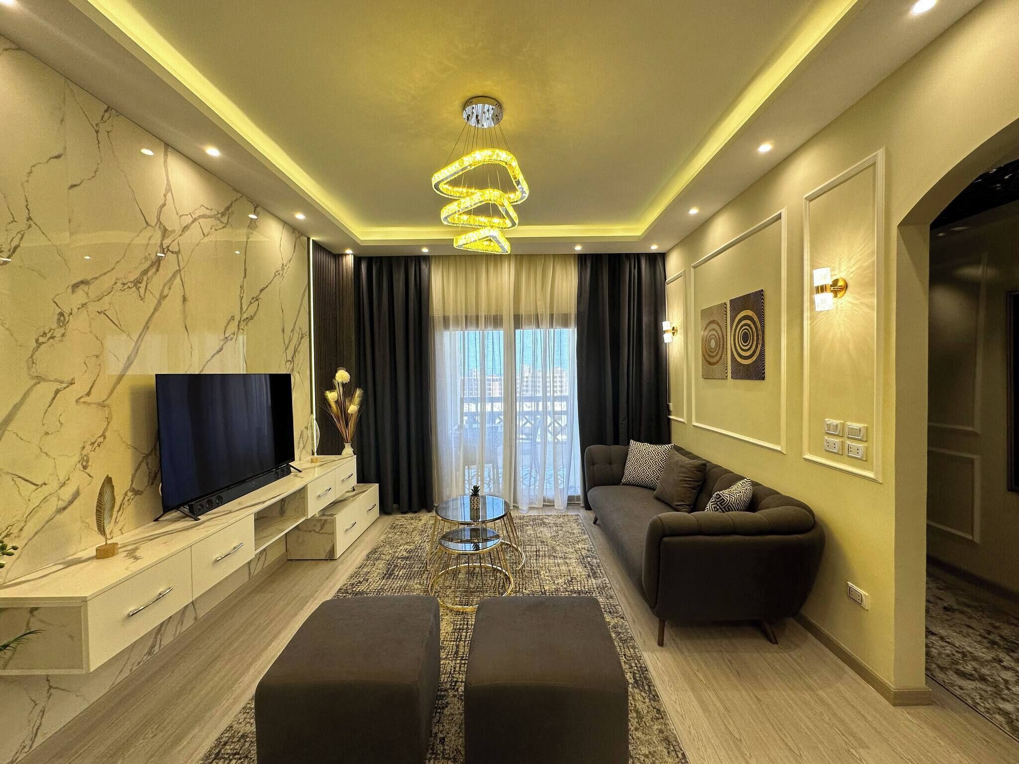A modern living room with a marble wall, a flat-screen TV, a sofa, and a unique chandelier.