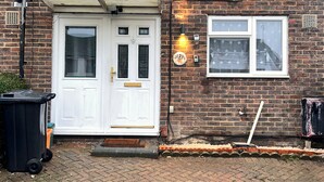 Une maison en briques avec une porte d’entrée blanche, une petite fenêtre et une plaque d’immatriculation.