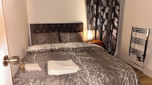 Un lit bien fait, avec une couvre-lit à motifs, une lampe de chevet et un radiateur.