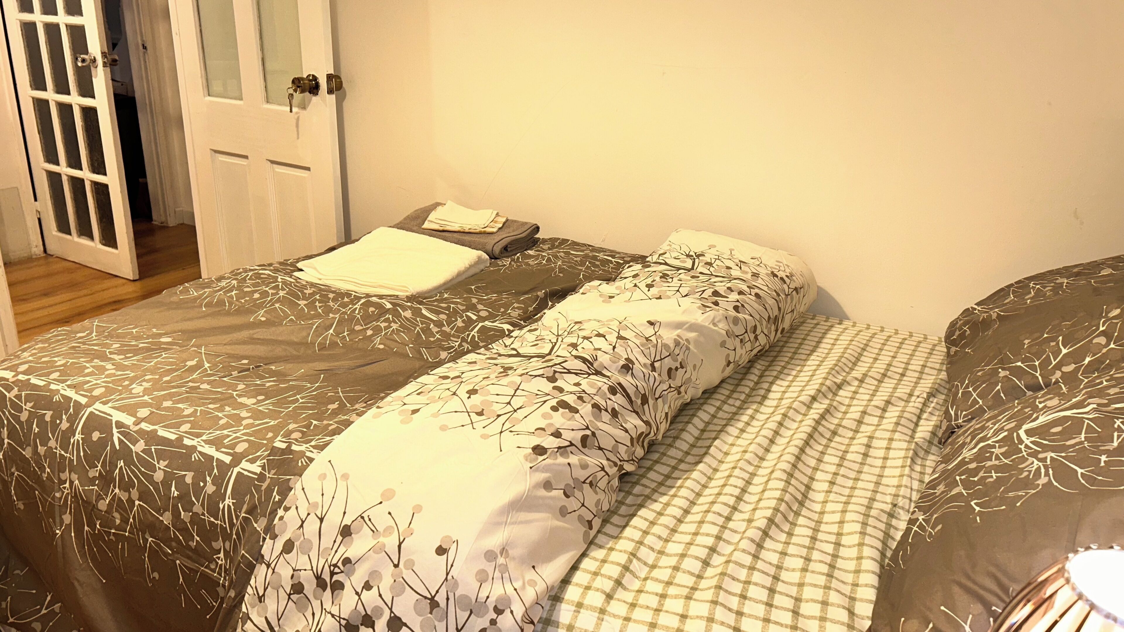 Une chambre avec deux lits, chacun recouvert d’une parure de lit à motifs. On y trouve une porte avec une clé dans la serrure, ainsi qu’une petite table sur laquelle est posée une serviette pliée.