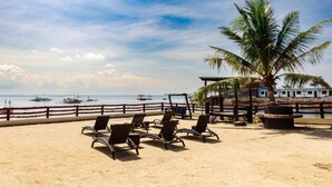 Una playa con sillones de baño, una palmera y barcos al fondo.