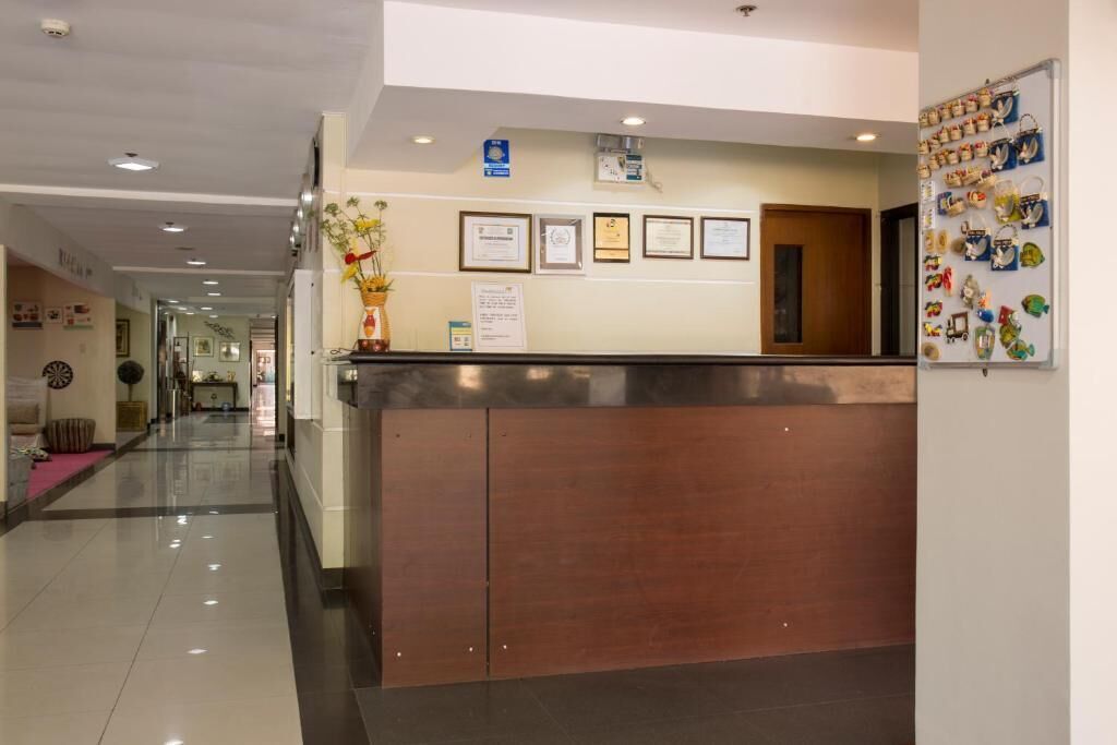 Zona de recepción de hotel con un mostrador de madera, certificados enmarcados en la pared y una vitrina con diversos objetos.