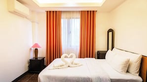 Una habitación de hotel con una cama, una mesita de noche, una lámpara, un espejo y cortinas.