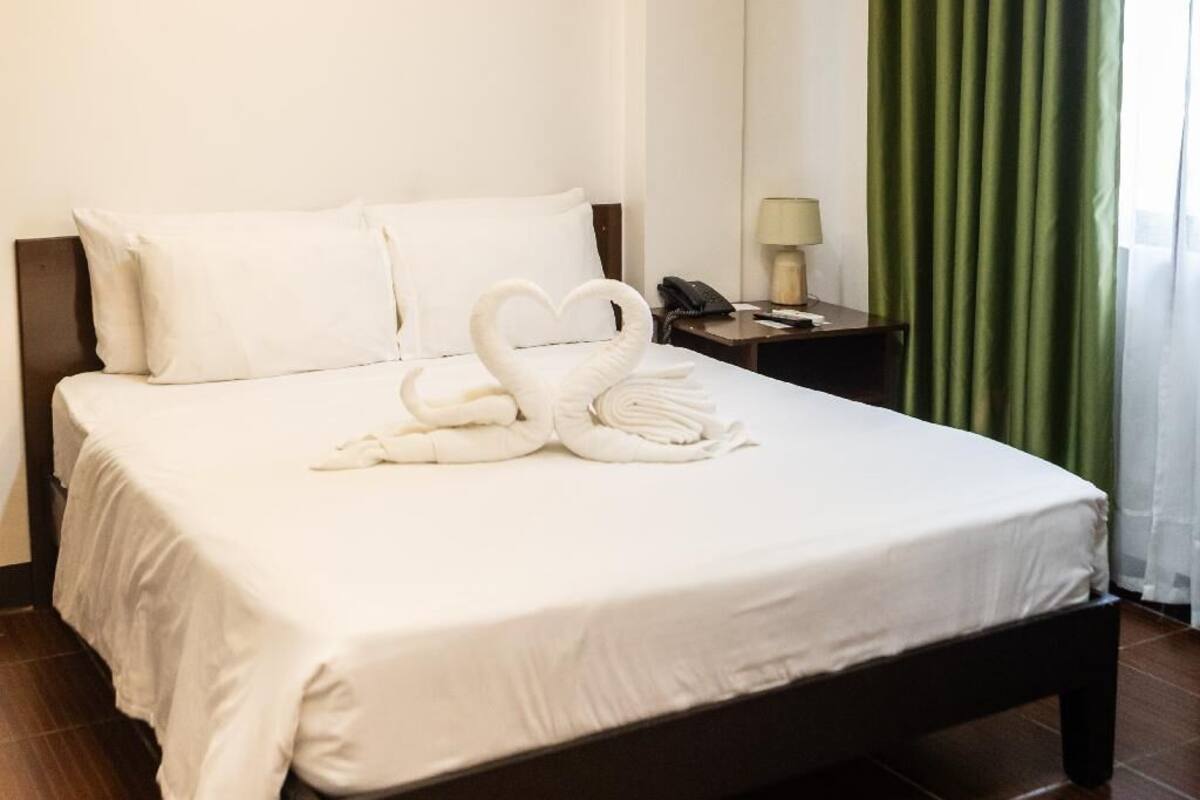 A hotel room with a bed, a nightstand, a lamp, and green curtains.