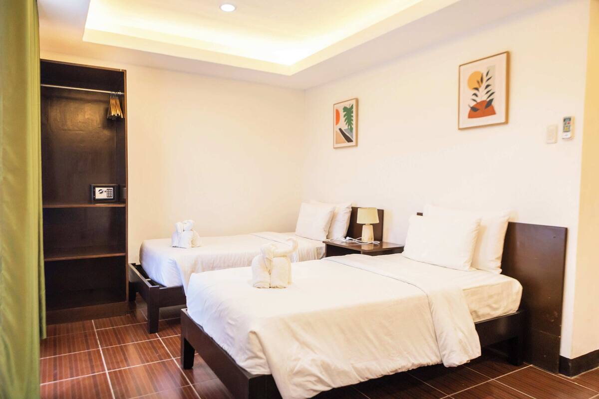A hotel room with two beds, a wardrobe, and a small desk with a lamp.