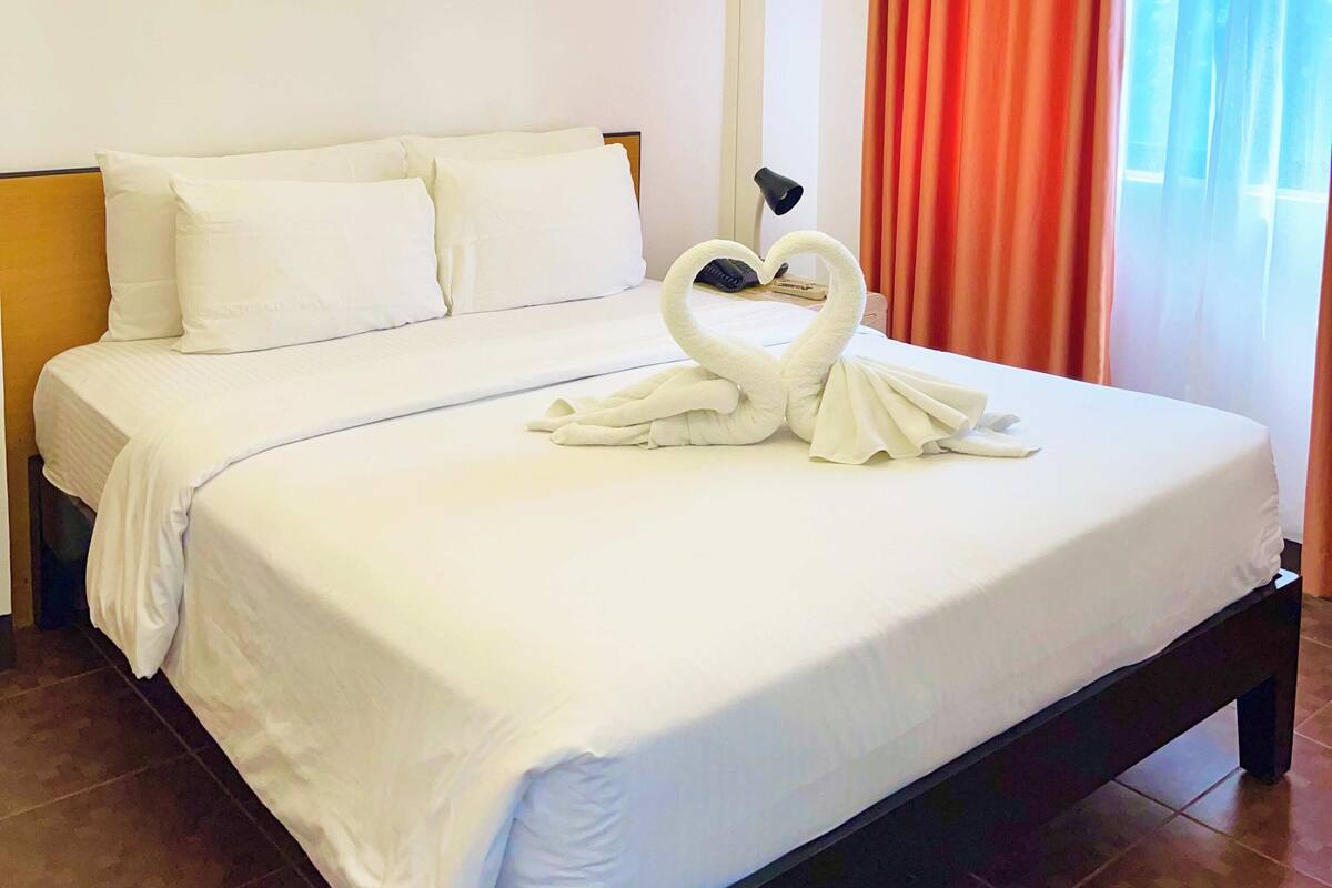 A neatly made bed with white linens and a heart-shaped towel arrangement on the bed.