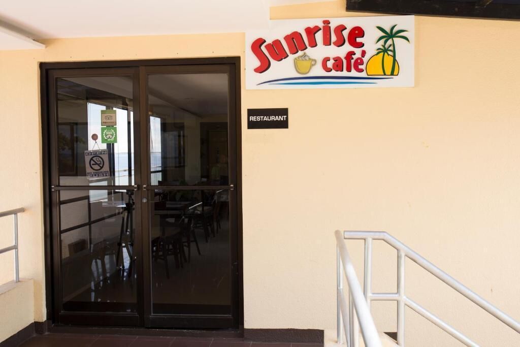 Entrada do Café Sunrise com porta de vidro, mesas internas e placa indicando ser um restaurante.