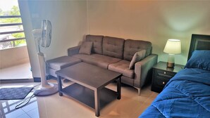 Een kamer met een bank, een klein tafeltje, een lamp en een bed.