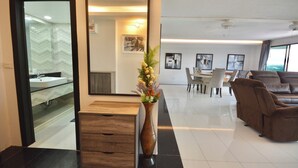 A modern hotel lobby with a reception desk, a large mirror, a vase with flowers, a dining area with chairs and a table, and a leather sofa. - One-Bedroom Sea-View Condo, 17th Floor – Angket, Jomtien (Muang Pattaya)