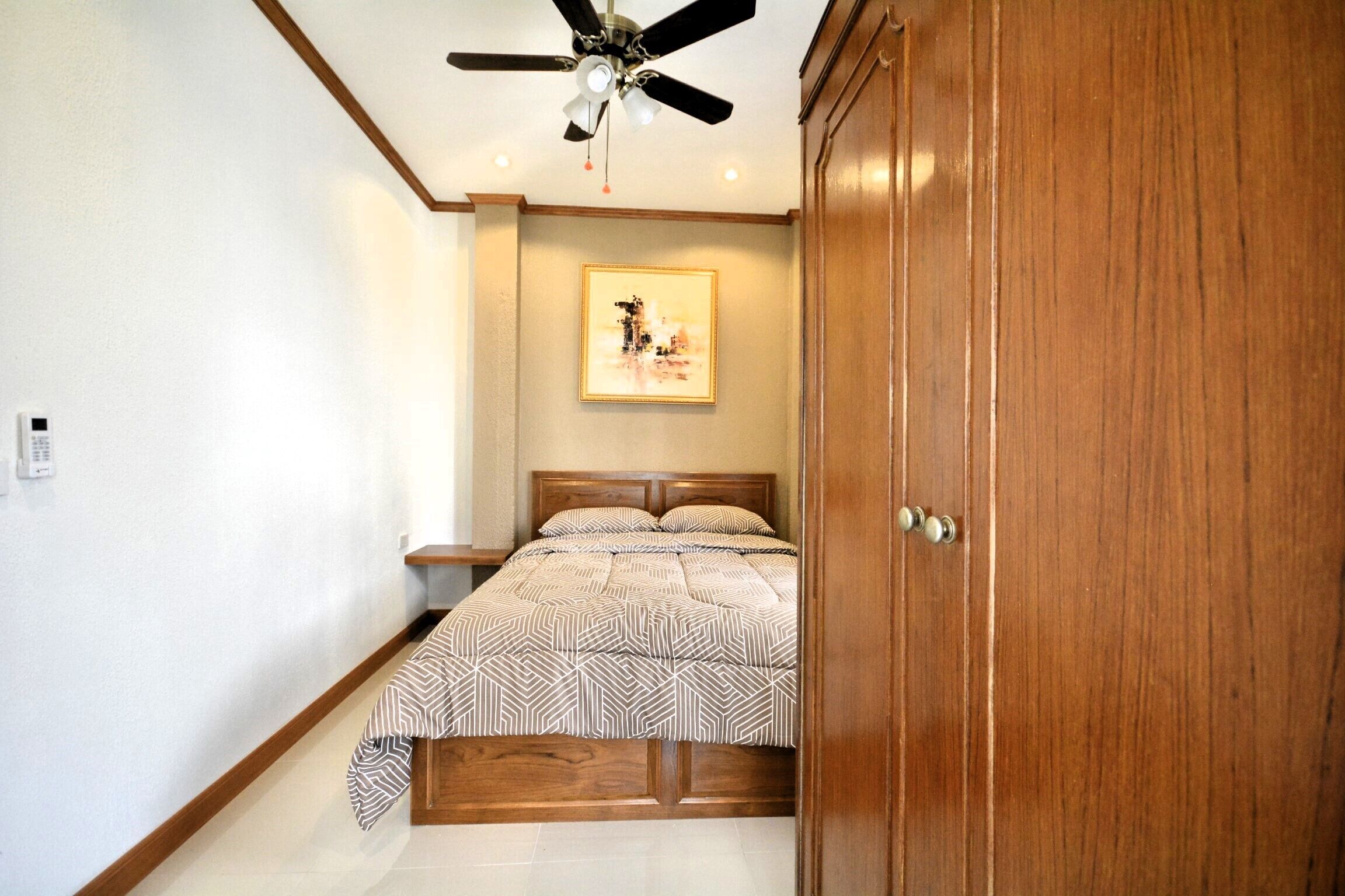 Une chambre à coucher comprenant un lit, un ventilateur de plafond, une table de chevet et une armoire en bois.