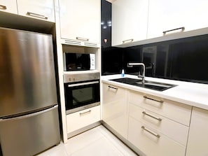 A modern kitchen with stainless steel appliances, a microwave, oven, and a sink. - Spacious 1-Bedroom Condo with Large Balcony at Baan Suan Lalana (Muang Pattaya)