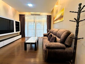 A living room with a flat-screen TV, a sofa, a coffee table, and a coat rack. - Spacious 1-Bedroom Condo with Large Balcony at Baan Suan Lalana (Muang Pattaya)