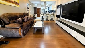 Ein modernes Wohnzimmer mit braunem Ledersofa, einem an der Wand montierten Fernseher und einer Essecke mit Barhocker.