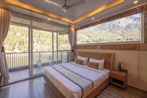 A bedroom with a large bed, a nightstand, and a view of a mountainous landscape through a large window. - Alaya Stays Lakefront Escape 2BHK Suite (Nainital)