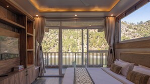 Un dormitorio con una cama grande, televisión y vistas a una ladera boscosa.