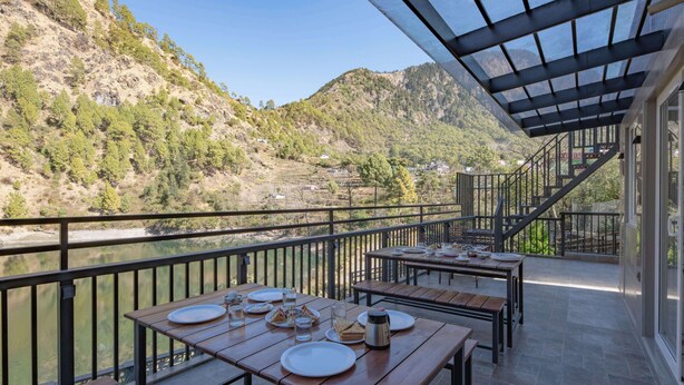 Una terraza con mesas dispuestas para comer, con vistas a un río y colinas.