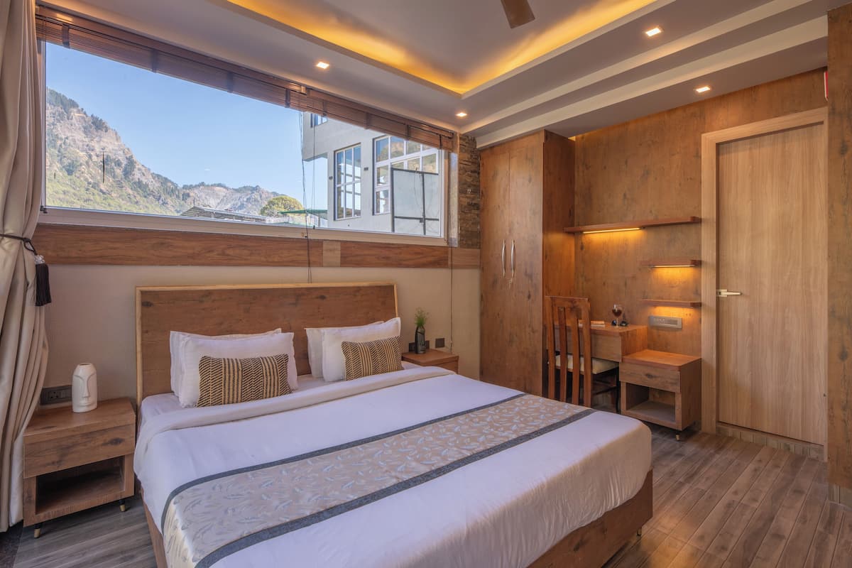 A modern hotel room with a large bed, wooden headboard, and a view of the mountains.