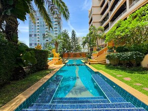 A swimming pool with a tiled deck, surrounded by lush greenery and a staircase leading to a building. - Spacious 2-Bedroom Pool-View Condo - Executive Residence 2, Pratumnak (Muang Pattaya)