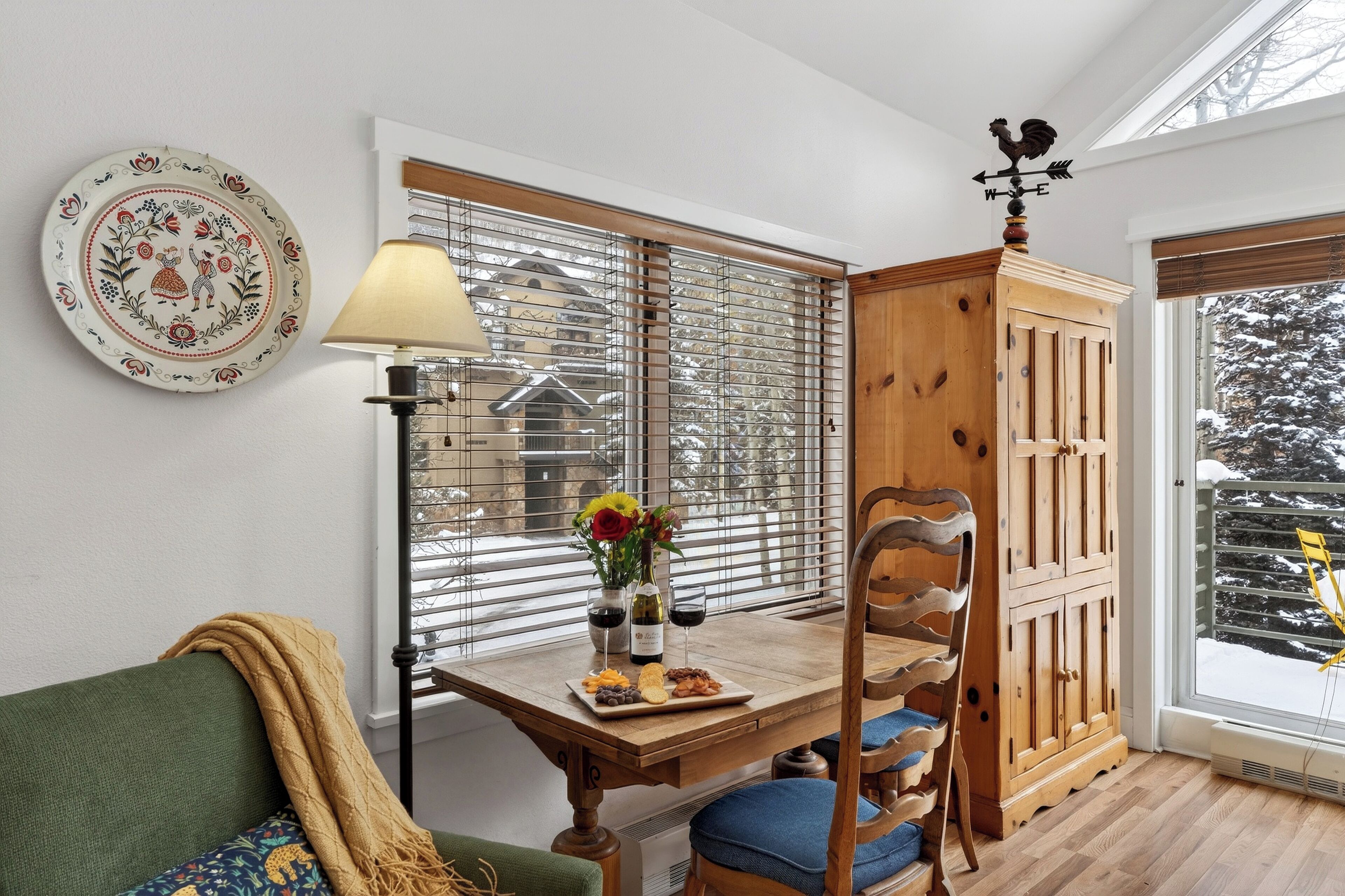Une pièce chaleureuse avec une table en bois dressée pour un repas, un canapé vert et une fenêtre avec des stores.