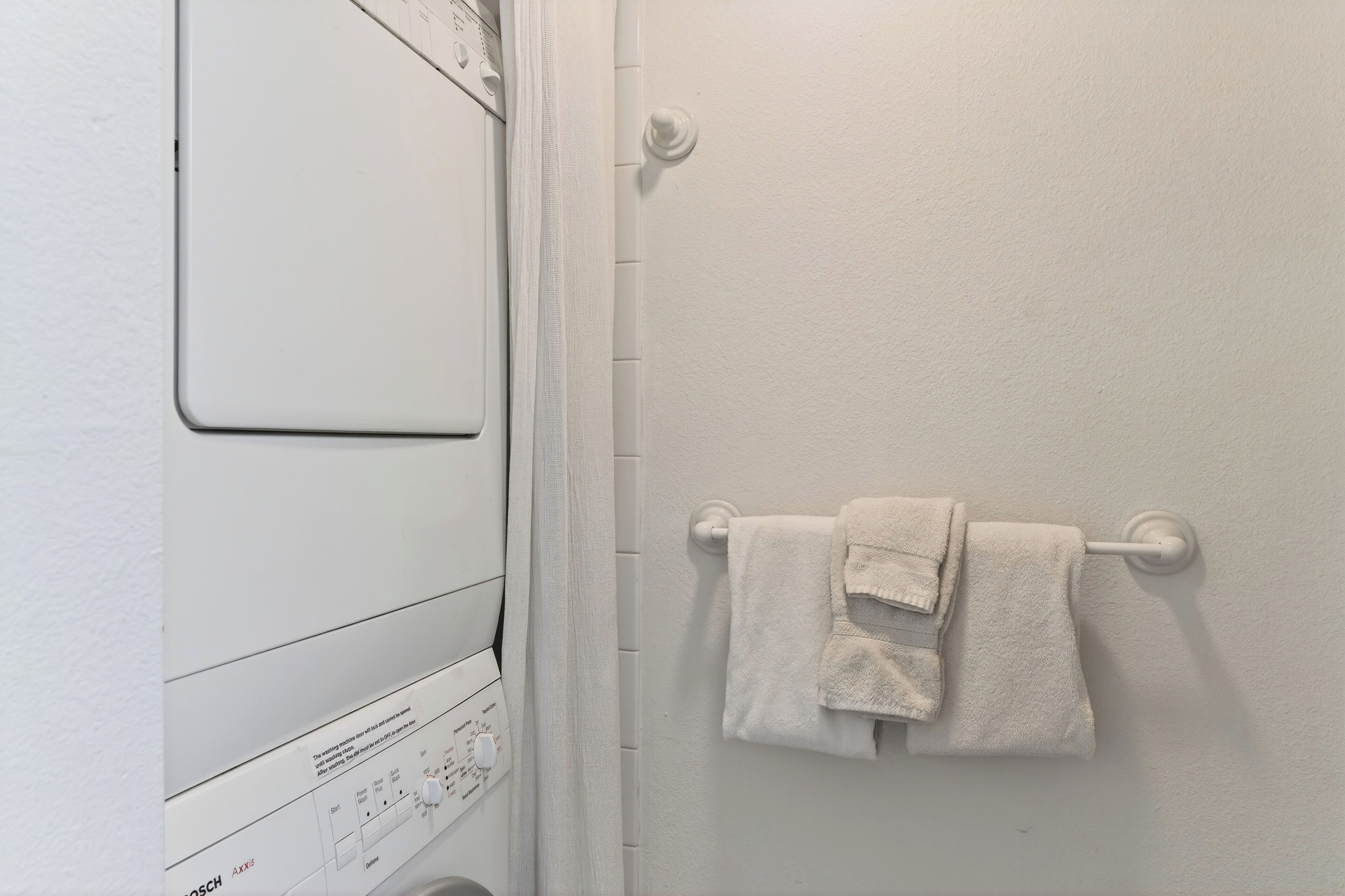 Pared blanca con una lavadora Bosch y un perchero con toallas dobladas.