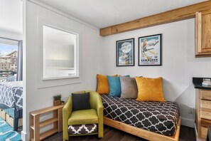 A bedroom with a bed, a green chair, a window, and two posters on the wall. - Prime Ski Access Condo, Walk to Gondola & Lifts | Blue Mesa Lodge (Mountain Village)