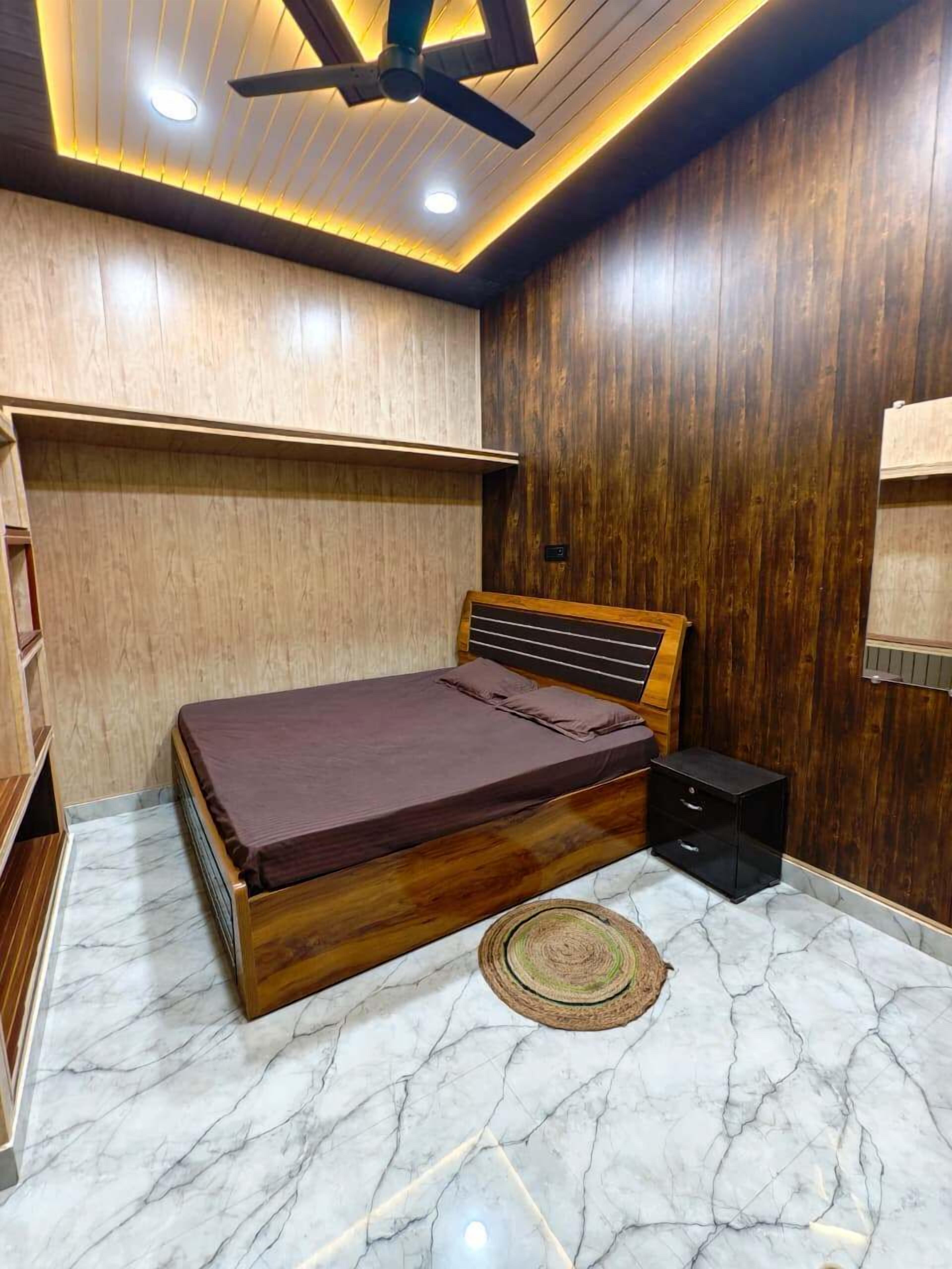 Ein Schlafzimmer mit einem hölzernen Bett, Marmorböden, einem Deckenventilator und integrierten Regalen.