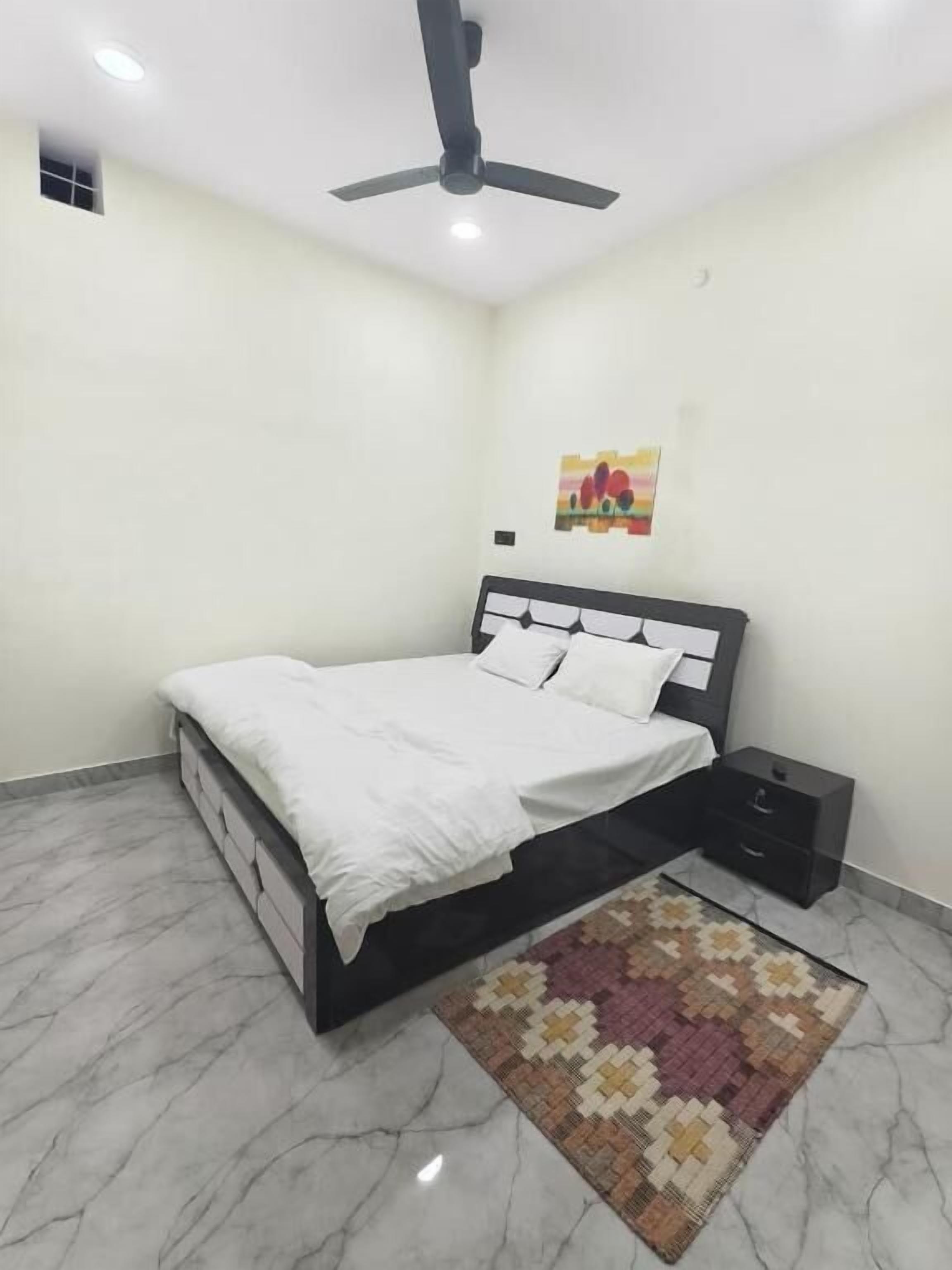 A bedroom with a bed, nightstand, ceiling fan, and a rug.