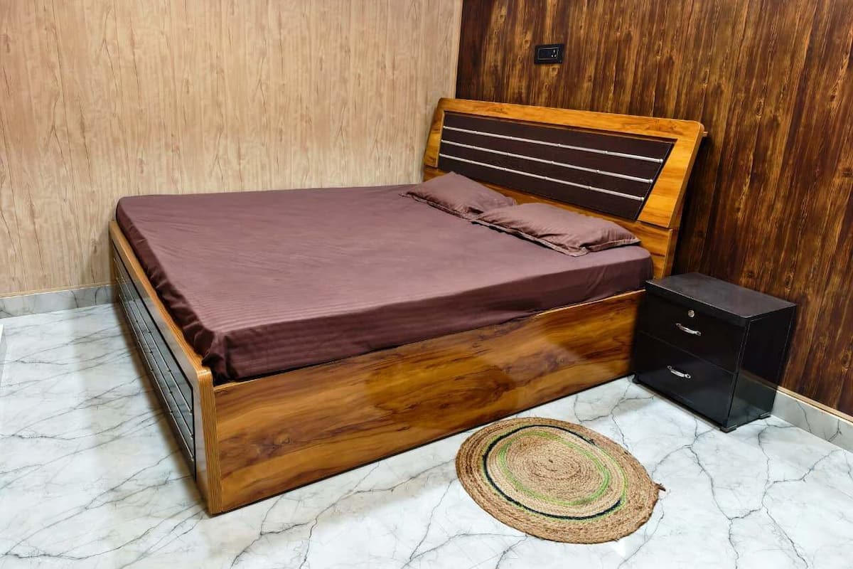 Ein Bett mit Holzkopfstück, einer dunkelgrauen Matratze und einem kleinen Nachttisch mit Schubladen.
