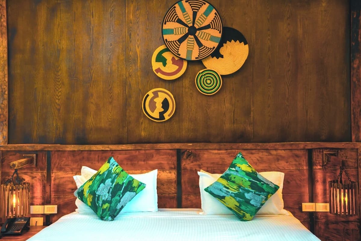 Una habitación de hotel con cabecera de madera, dos almohadas con diseños abstractos y un muro decorado con motivos circulares.