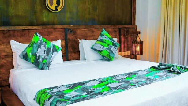 Un grand lit avec un cadre en bois, une literie blanche et des oreillers à motifs verts et blancs.