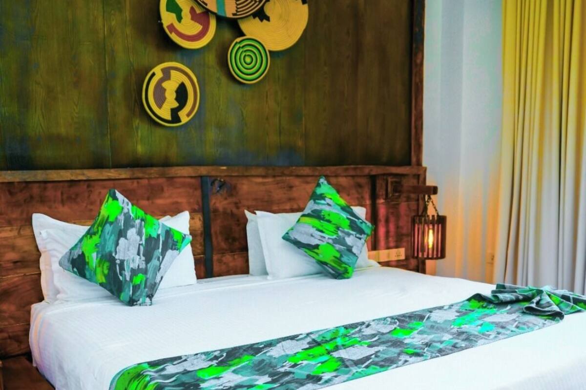 Una cama grande con estructura de madera, ropa blanca y almohadas con estampado verde y blanco.