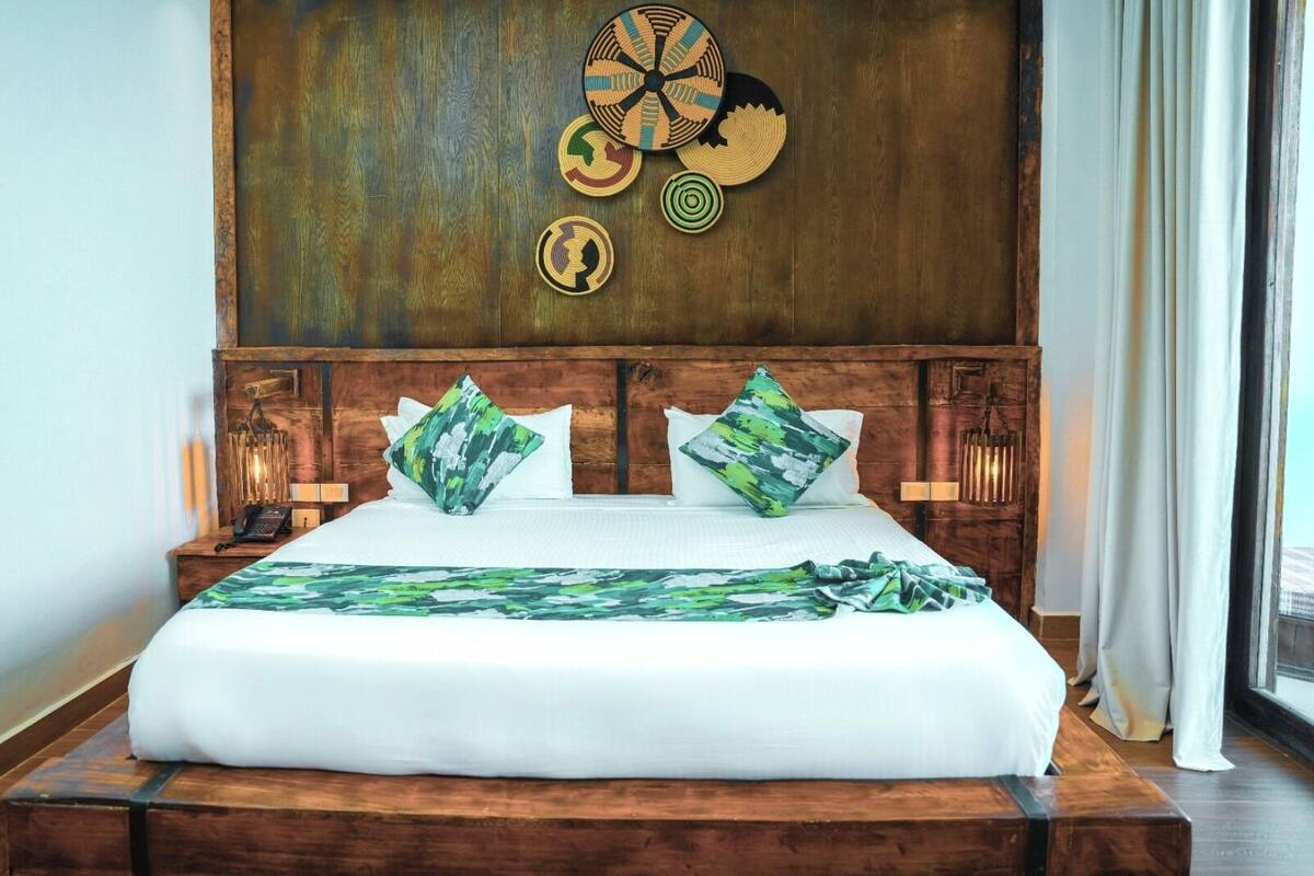 Una cama grande con cabecera de madera, dos almohadas verdes estampadas y una colcha blanca.