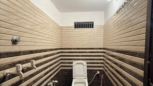 A small, narrow bathroom with a toilet, a showerhead, and a handwashing station.