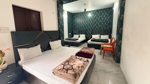 A bedroom with a large bed, a desk, and a chair. There is a wardrobe and a mirror. The room has a patterned wallpaper and a ceiling fan.