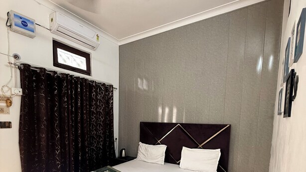 A neatly arranged bedroom with a bed, a ceiling fan, an air conditioning unit, and a window with curtains.