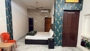 A compact bedroom with a bed, a small table, and a chair. There is a wardrobe and a door with a sign above it.