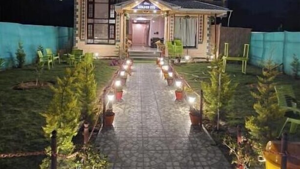 A building with a central entrance, flanked by potted plants and lights, leading to a covered area. - Hotel Golden Eye (Srinagar)